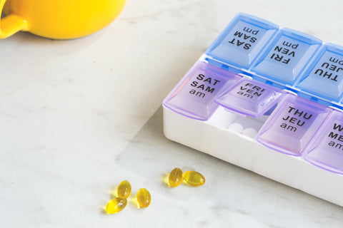 una taza de color amarillo y perlas de aceite y un pastillero sobre un fondo blanco 